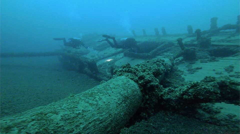 2 divers swimming across an old wooden shipwreck