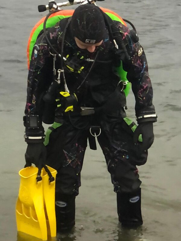 dui clx450 multicolour drysuit worn by dive shop staff member Ross wearing it with yellow jet fins, kubi dry glove cuffs, orange, yellow and green double tank with with a pair of double faber 100 cubic foot tanks